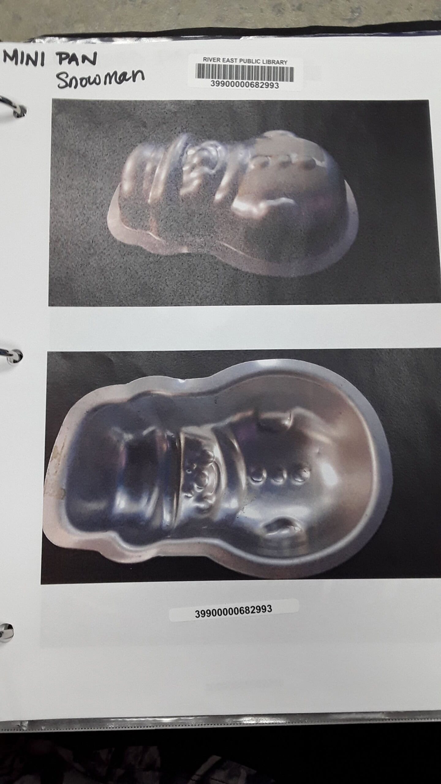 Two photos of a metallic snowman-shaped baking pan are shown on a page in a binder. The top photo shows the pan at an angle, while the bottom photo displays the front with facial and button details visible.