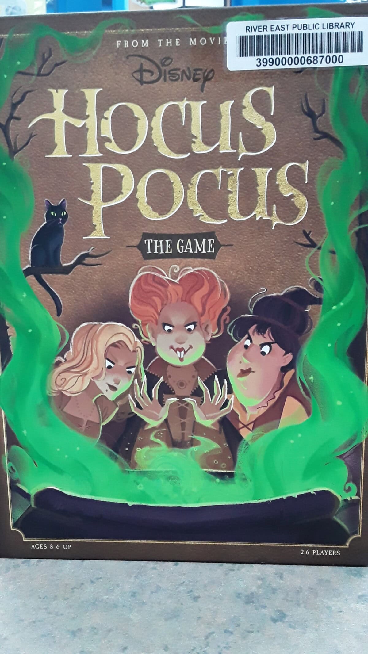 Front cover of Disney Hocus Pocus: The Game showing three cartoon witches surrounded by green smoke, with a black cat on the left. The box is labeled for ages 8+ and 2-6 players.