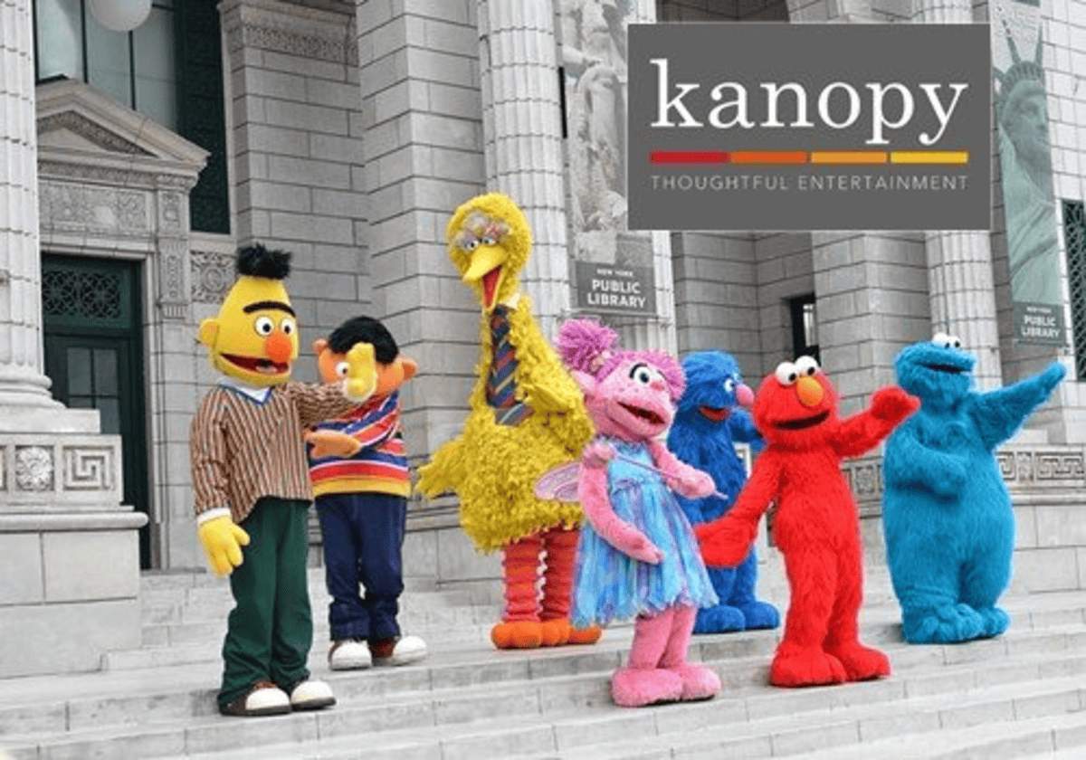 Costumed characters from Sesame Street, including Bert, Ernie, Big Bird, Abby Cadabby, Elmo, and Cookie Monster, stand on the steps of a public library. A Kanopy logo appears in the top right corner.