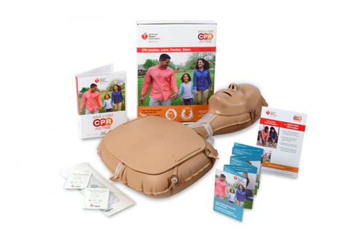 CPR training kit with a practice manikin, instructional booklets, cards, practice sheets, and a box featuring adults and a child on the cover. Items are arranged on a white background.