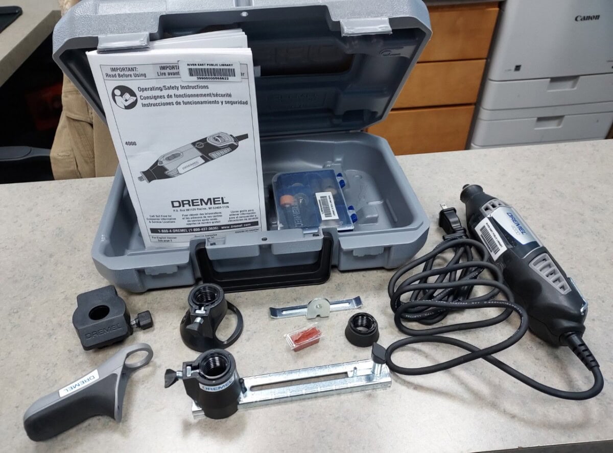 A Dremel rotary tool kit on a counter, including the tool, various attachments, accessories, a wrench, instruction manual, and a gray plastic carrying case.
