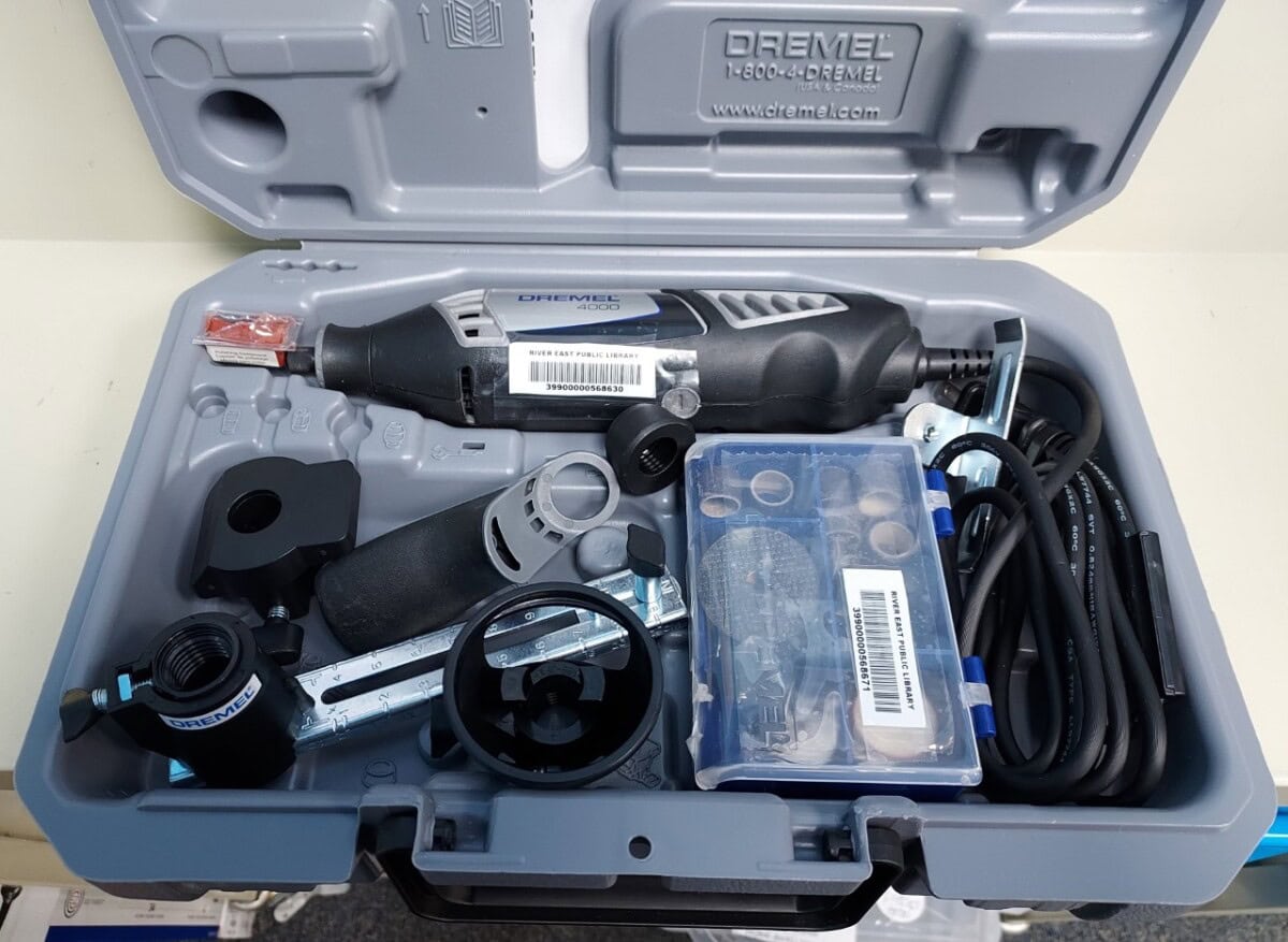A Dremel rotary tool kit inside a gray plastic case, including the main tool, attachments, accessories, a plastic box of bits, a power cord, and instruction manuals.