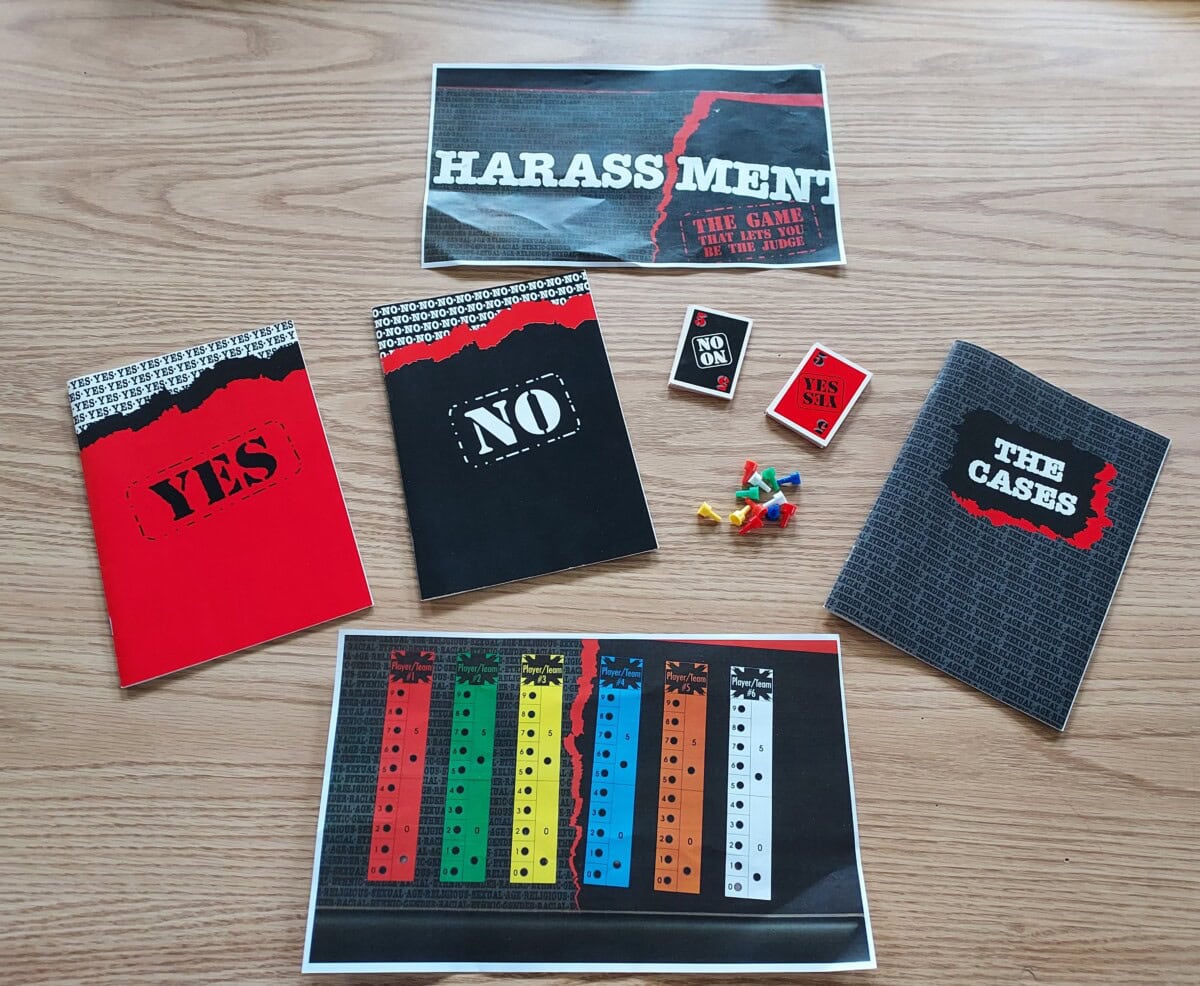 A board game called Harassment is displayed on a wooden surface, showing cards labeled YES, NO, and THE CASES, colored boards, pins, and tokens, along with the game’s title sheet.