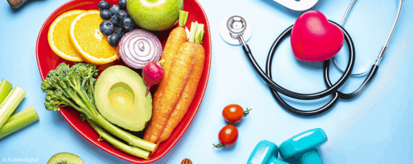 A heart-shaped bowl filled with fruits and vegetables, next to a stethoscope with a heart-shaped object, two tomatoes, blue dumbbells, and a glucometer on a blue background.