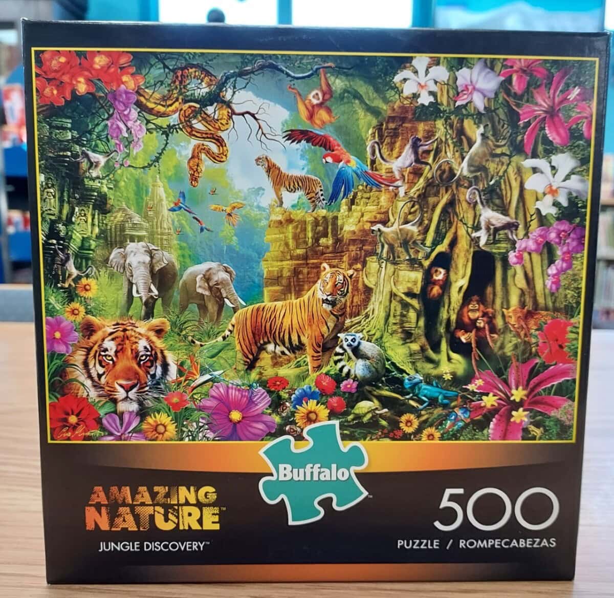 A colorful 500-piece puzzle box titled Amazing Nature: Jungle Discovery features vibrant images of jungle animals, including tigers, monkeys, parrots, and a waterfall, surrounded by lush greenery and flowers.