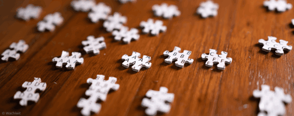 Several jigsaw puzzle pieces scattered on a wooden surface. Each piece is labeled with letters such as A, B, C, and D instead of a traditional puzzle image.