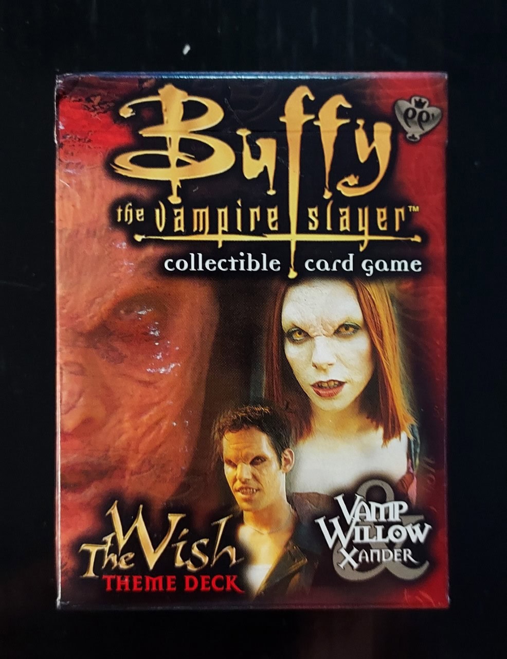 A box for the Buffy the Vampire Slayer collectible card game, featuring characters Willow and Xander with vampiric appearances. The box reads “The Wish Theme Deck” with a dark, dramatic design.