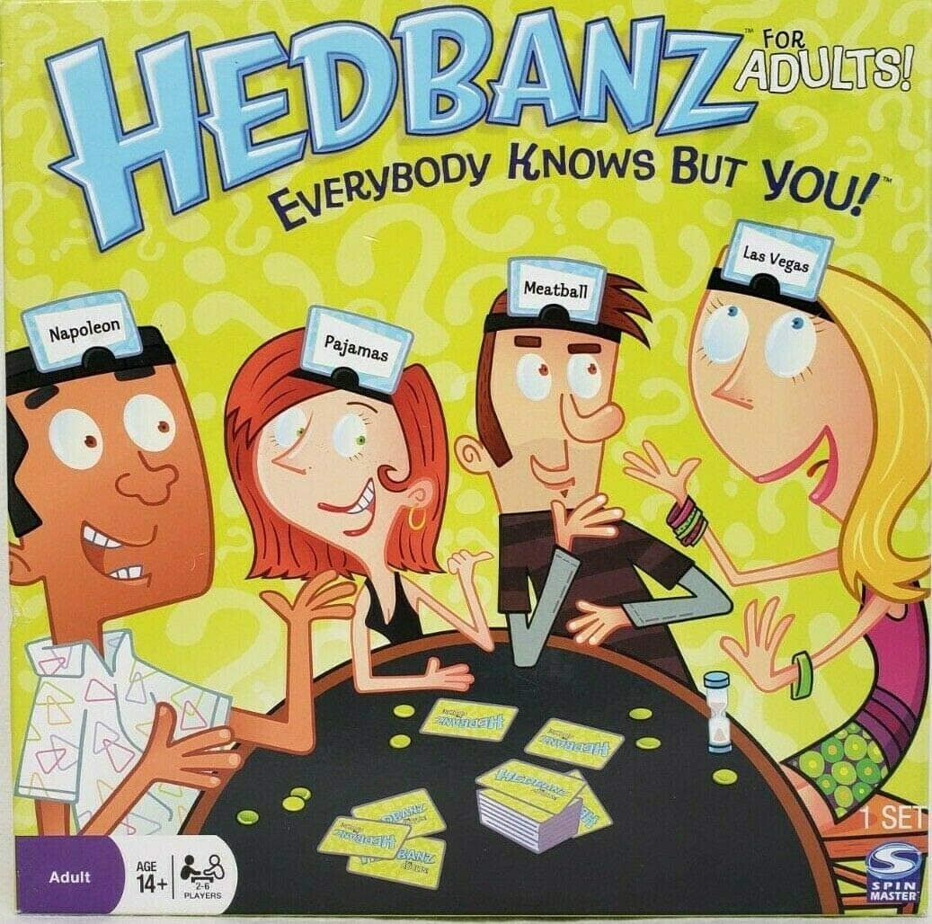 Four cartoon adults play Hedbanz, each with a headband showing a card: Napoleon, Pajamas, Meatball, and Las Vegas. They sit around a table with cards, laughing and gesturing. The game box reads Hedbanz for Adults!.