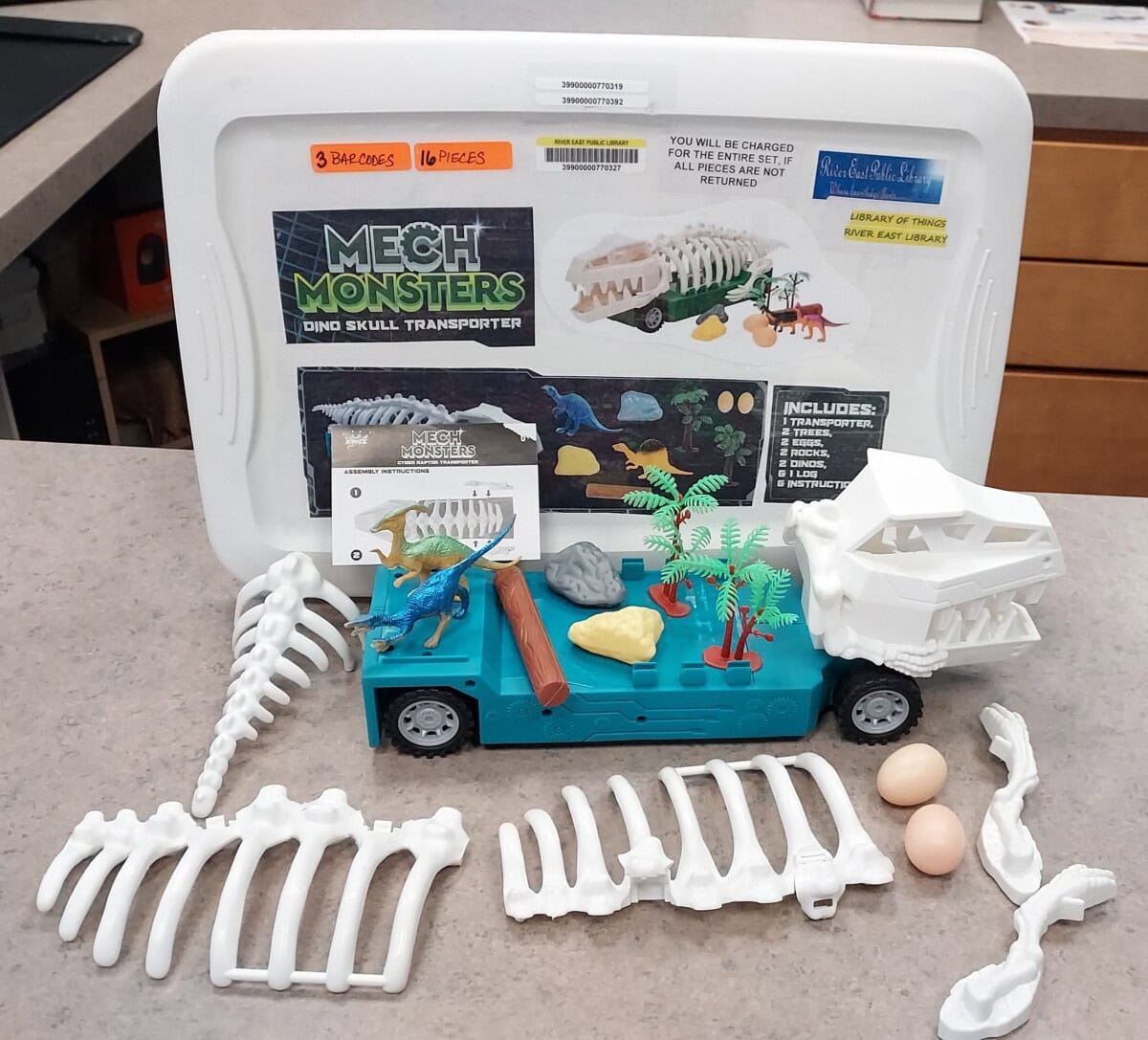 A Mech Monsters Dino Skull Transporter toy set with plastic dinosaur bones, eggs, small dinosaur figures, and accessories arranged on a countertop in front of the set’s storage case.