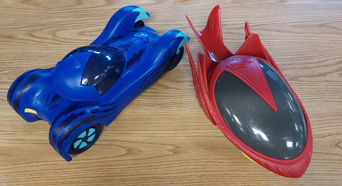 Two toy vehicles on a wooden surface: one is a sleek blue car with turquoise accents, the other is a red and gray futuristic vehicle with fin-like structures.