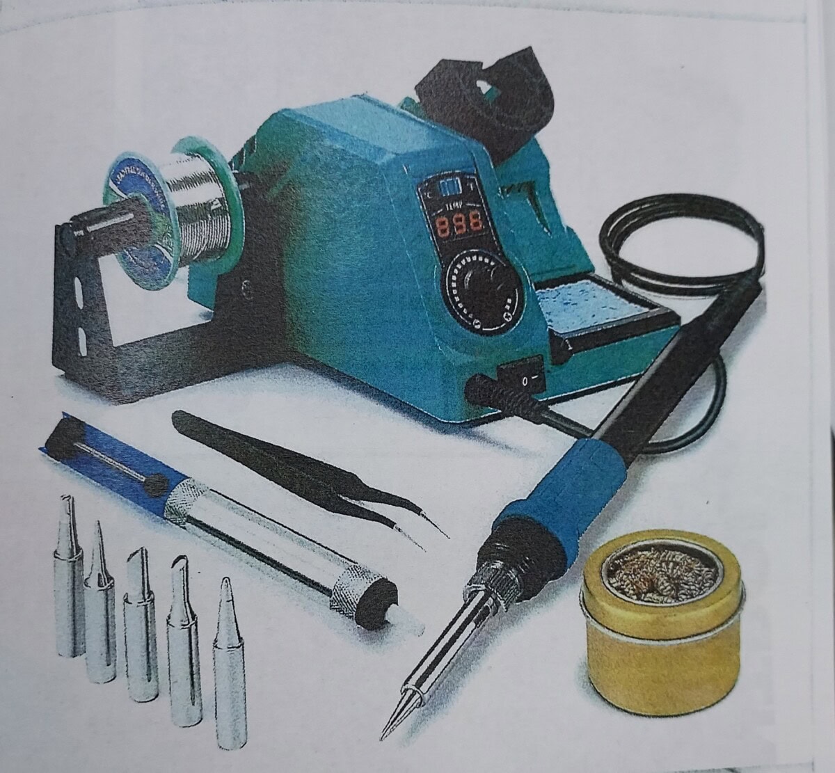 A digital soldering station with a blue handle, soldering tips, solder wire spool, tweezers, solder sucker, cleaning sponge, and brush, arranged neatly on a white surface.
