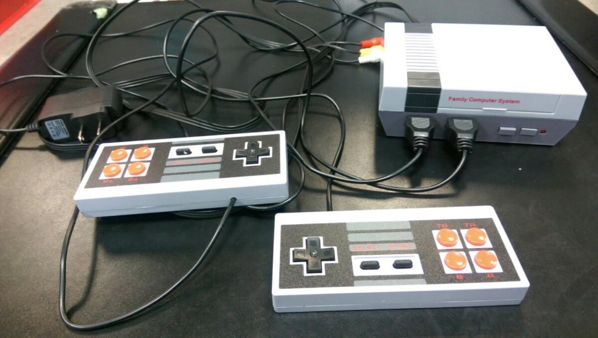 A retro gaming console labeled Family Computer System sits on a table, connected to two classic-style rectangular controllers with black and orange buttons and joysticks, along with AV and power cables.