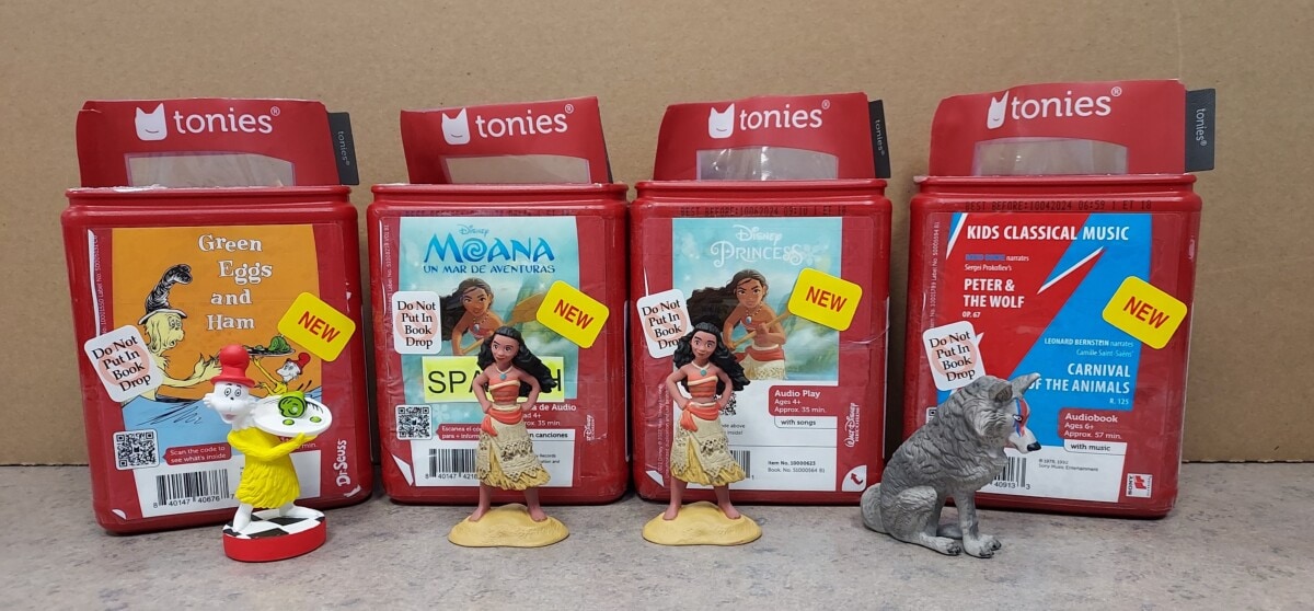 Four red Tonies audio character boxes are displayed in a row, featuring Green Eggs and Ham, Moana, Disney Princess, and Kids Classical Music, each with figurines of Moana, the Cat in the Hat, and a wolf in front.