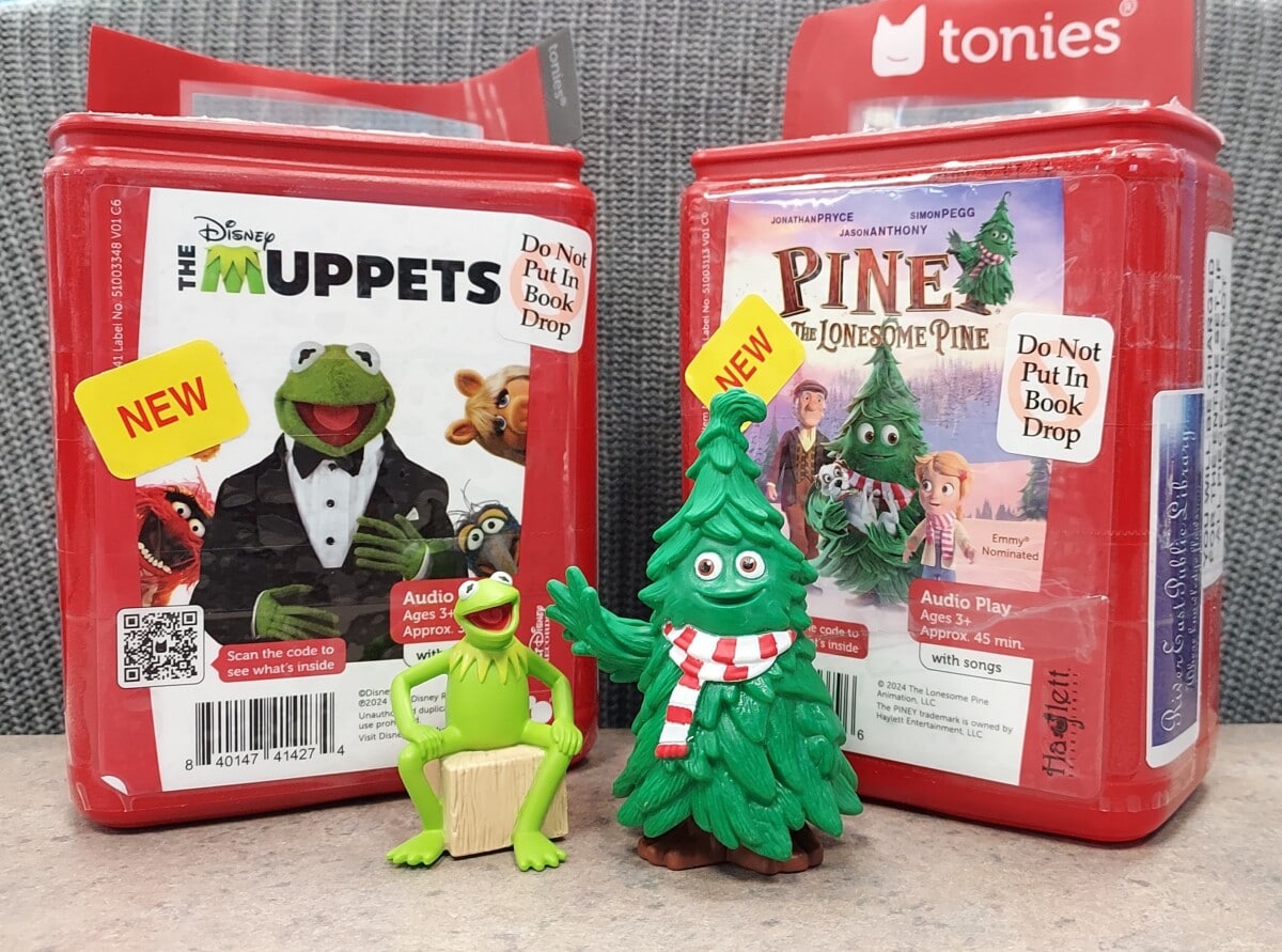 Two red Tonies audio book boxes stand side by side. The left box features The Muppets; the right features Pine and The Lonesome Pine. In front are Kermit the Frog and a smiling pine tree figurine.