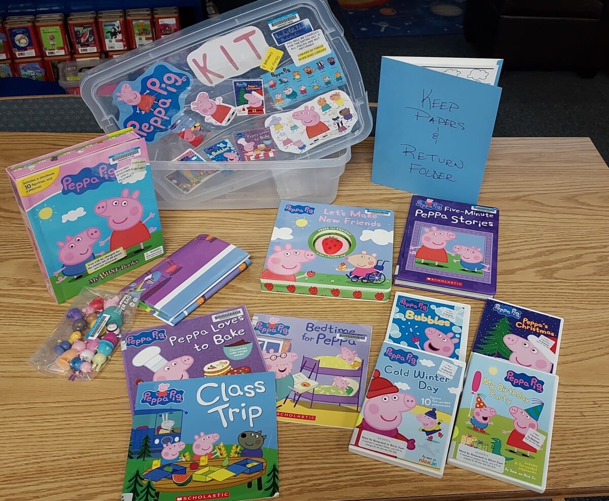A table displays a Peppa Pig-themed kit with books, a folder, DVDs, character figurines, and a plastic storage bin labeled “Peppa Pig Kit.” A blue folder says “Keep Papers & Return Folder.”.