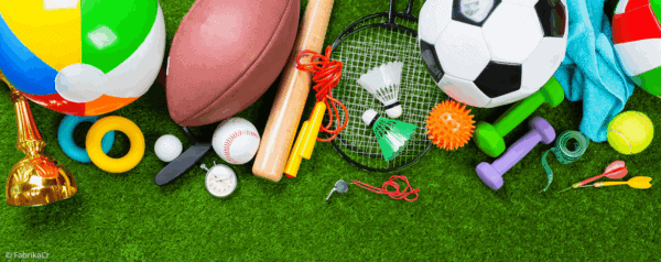 Various sports equipment, including a soccer ball, football, baseball, beach ball, badminton racket and shuttlecocks, dumbbells, stopwatch, darts, tennis racket, jump rope, and trophies, arranged on green grass.