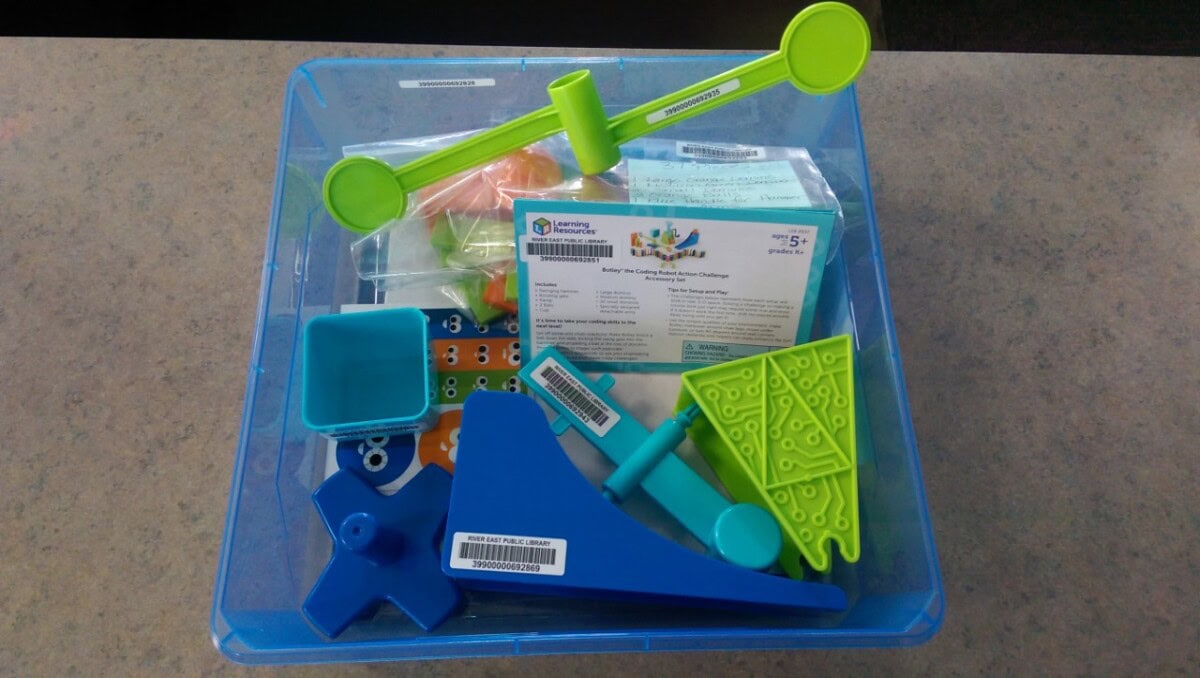 A blue plastic bin containing various colorful STEM activity tools, such as levers, counters, cards, and connectors, along with instruction sheets and plastic bags, sits on a gray surface.