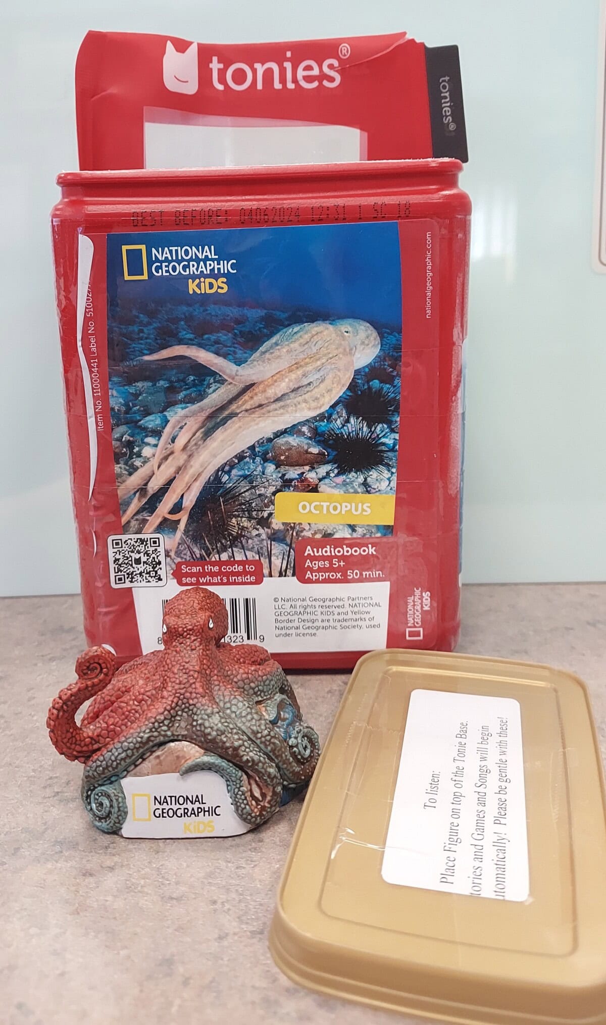 A red Tonies audio box with National Geographic Kids Octopus cover, a small octopus figurine, and a tan lid with a label, all placed on a white surface.