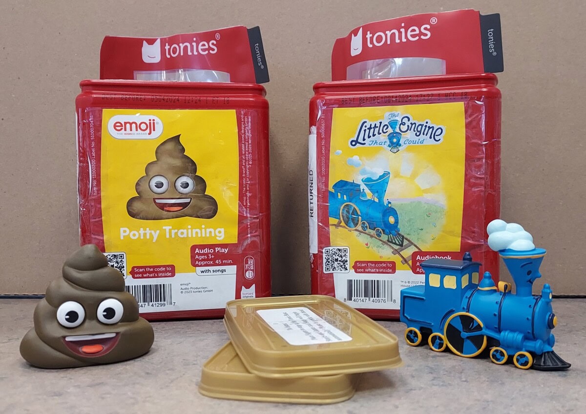Two Tonies audio boxes are shown: one for Emoji Potty Training with a poop emoji, and one for Little Engine That Could with a blue train. A poop emoji figure, a blue toy train, and a gold container are in front.