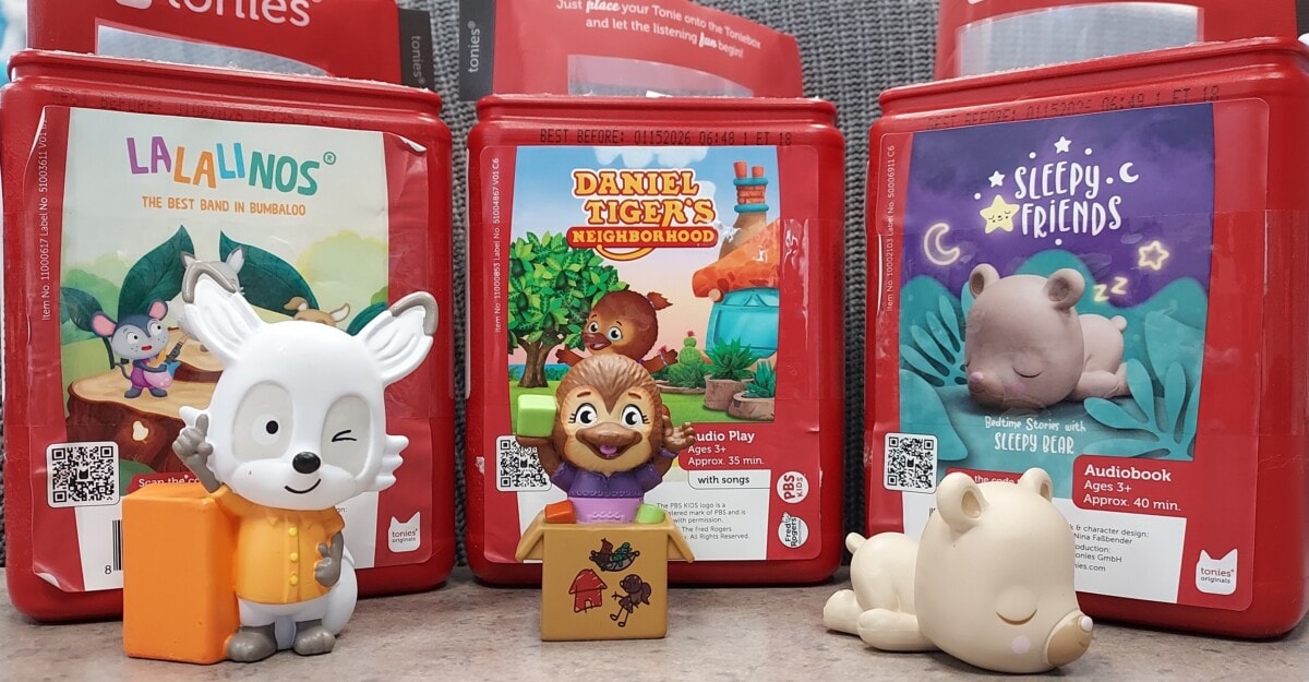 Three red audio book boxes labeled Lalalinos, Daniel Tigers Neighborhood, and Sleepy Friends stand behind matching animal figures: a fox, a lion, and a bear, with gray fabric in the background.