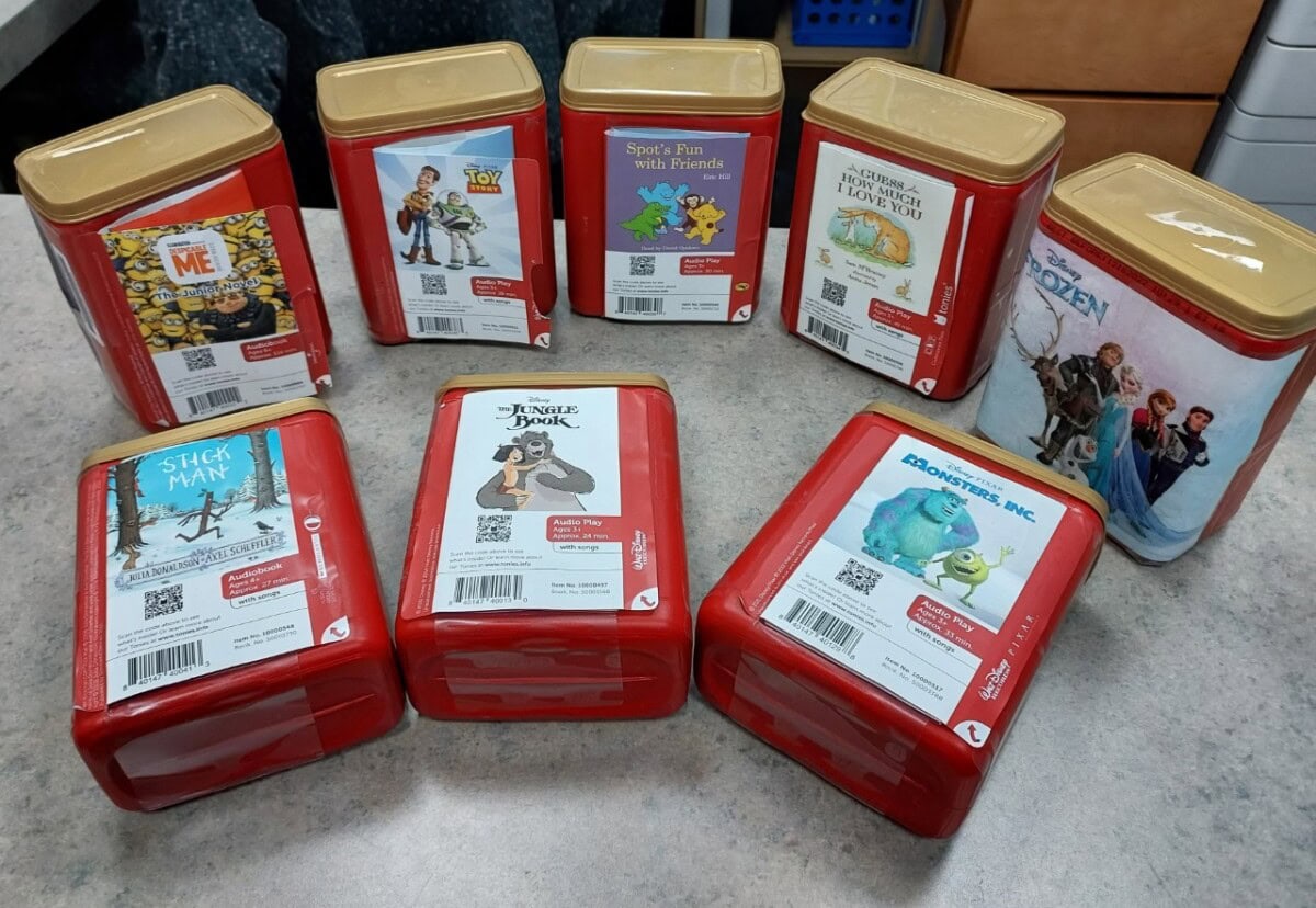 Seven red and gold rectangular containers with labels featuring Disney and animated movie characters, such as Frozen, Toy Story, Monsters, Inc., and The Jungle Book, arranged on a gray countertop.