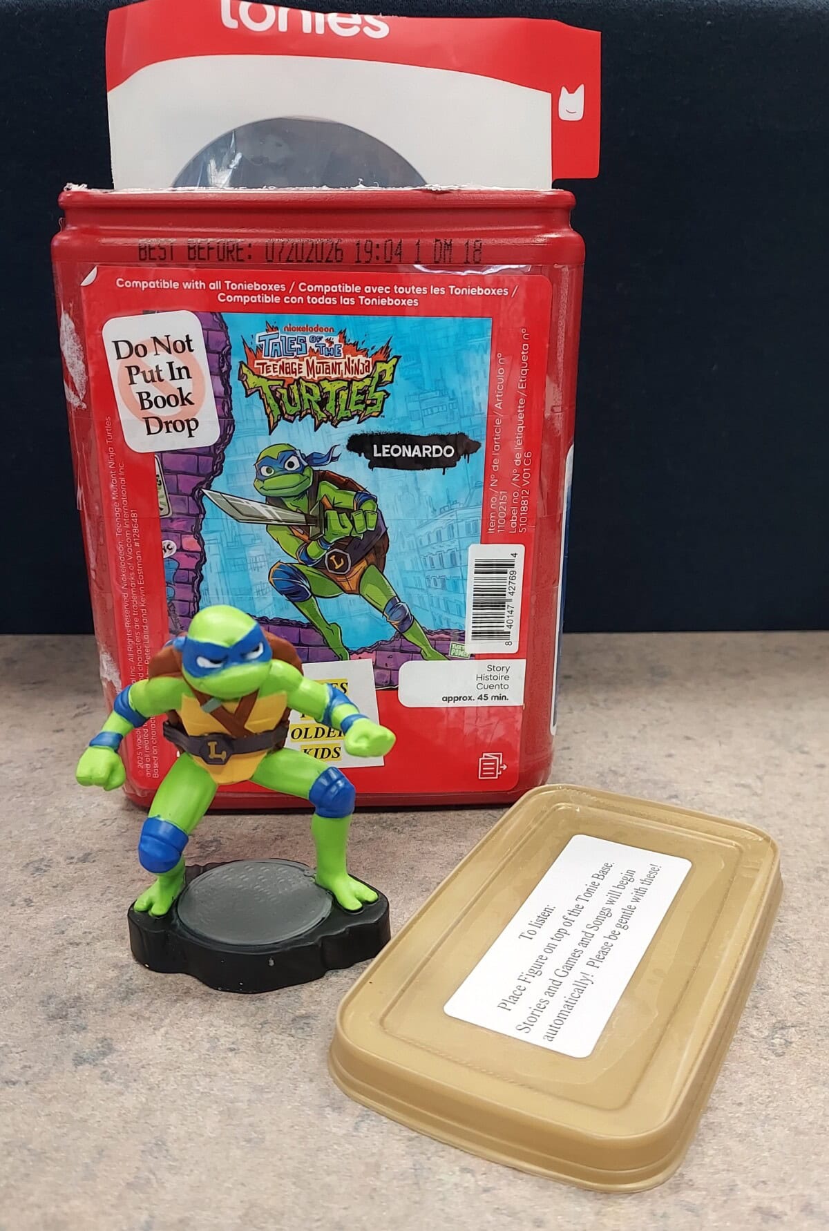Leonardo action figure from Teenage Mutant Ninja Turtles, displayed on a black base with a red box featuring character artwork.
