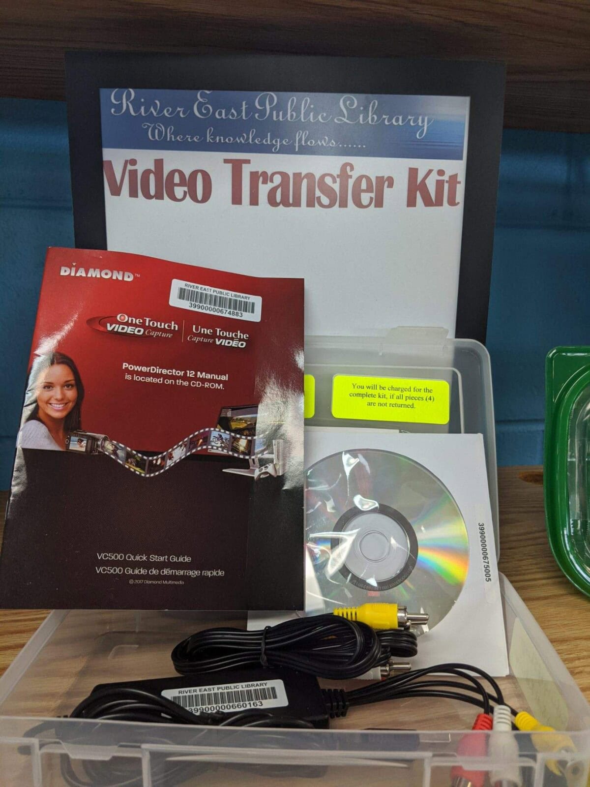 A video transfer kit from River East Public Library, including a guide with a smiling woman on the cover, a CD, and various cables neatly arranged in a clear plastic case.